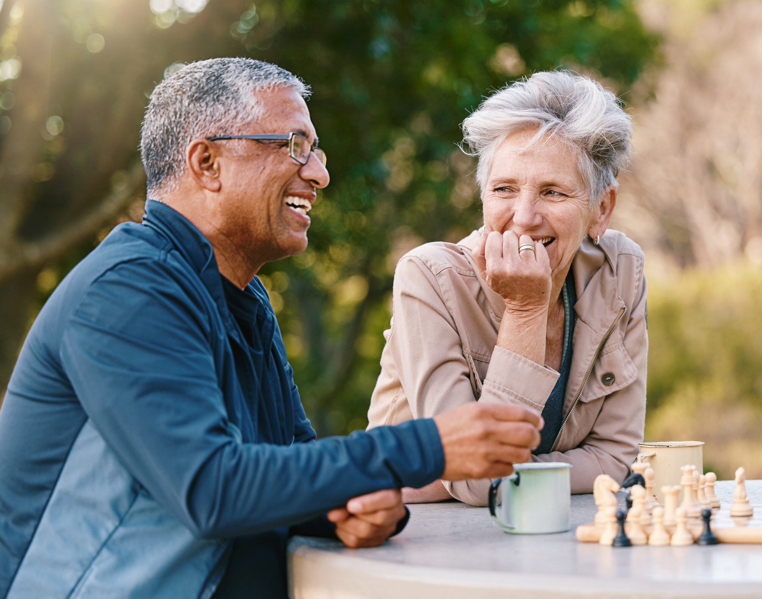 Happy, healthy, senior friends in nature playing a board game, bonding or talking about a funny story.